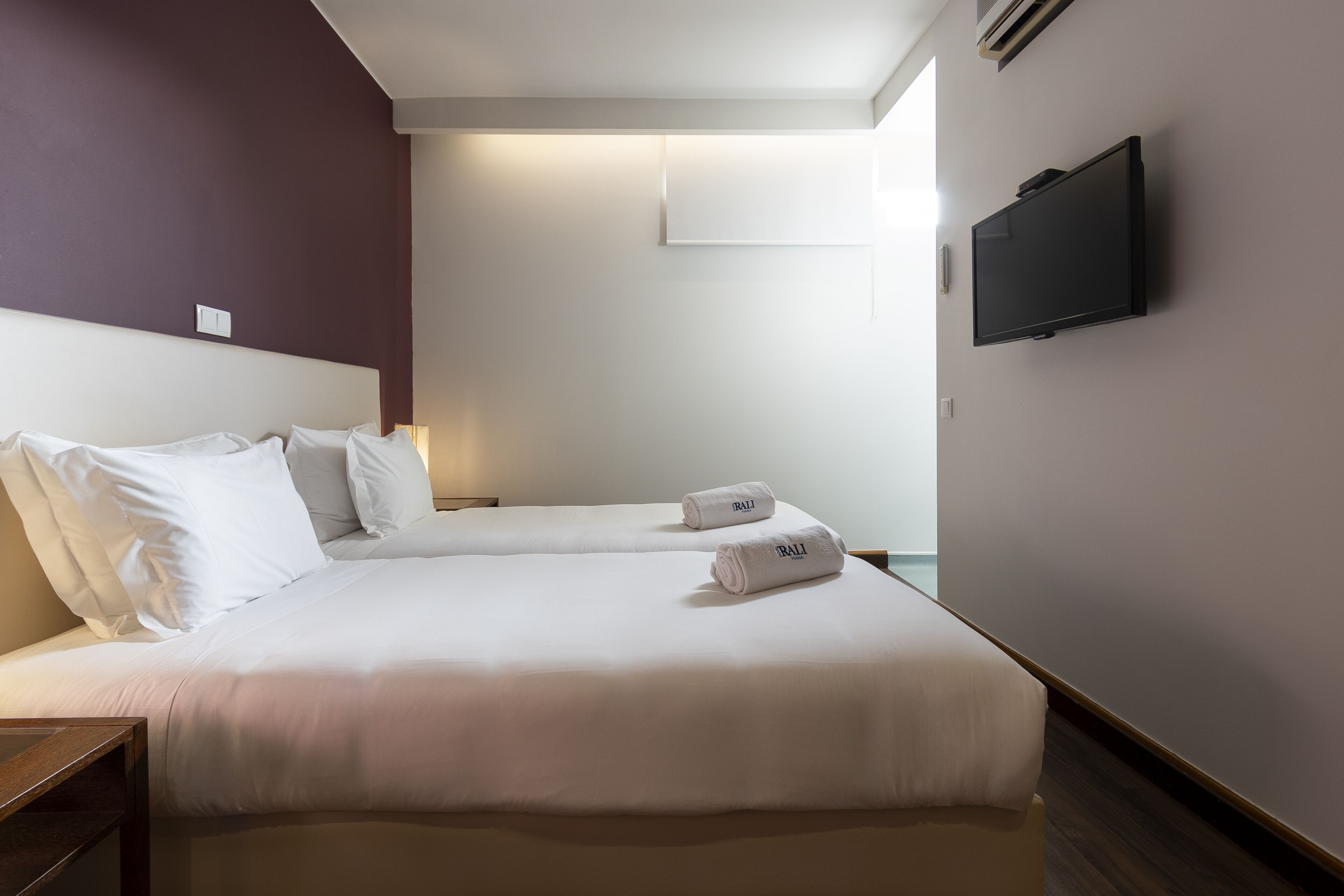 A hotel room with two beds, a flat-screen TV mounted on the wall, and a small table.