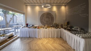 Una mesa de buffet, larga y cubierta con tela blanca, rodeada de diversos alimentos y bebidas.