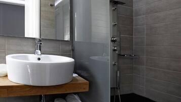 Un baño moderno con un lavabo blanco redondo, un espejo y una ducha con mampara de vidrio.