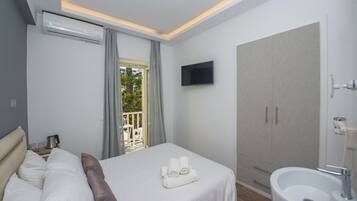 A hotel room with a bed, a TV mounted on the wall, a wardrobe, a bathroom with a sink, and a window with curtains.