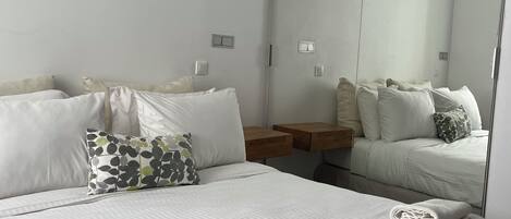 A modern hotel room with a large bed, a wooden nightstand, a mirror, and a view of the city.