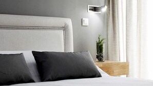 Una habitación de hotel moderna con una cama grande, una mesita de noche con lámpara y vistas al exterior.