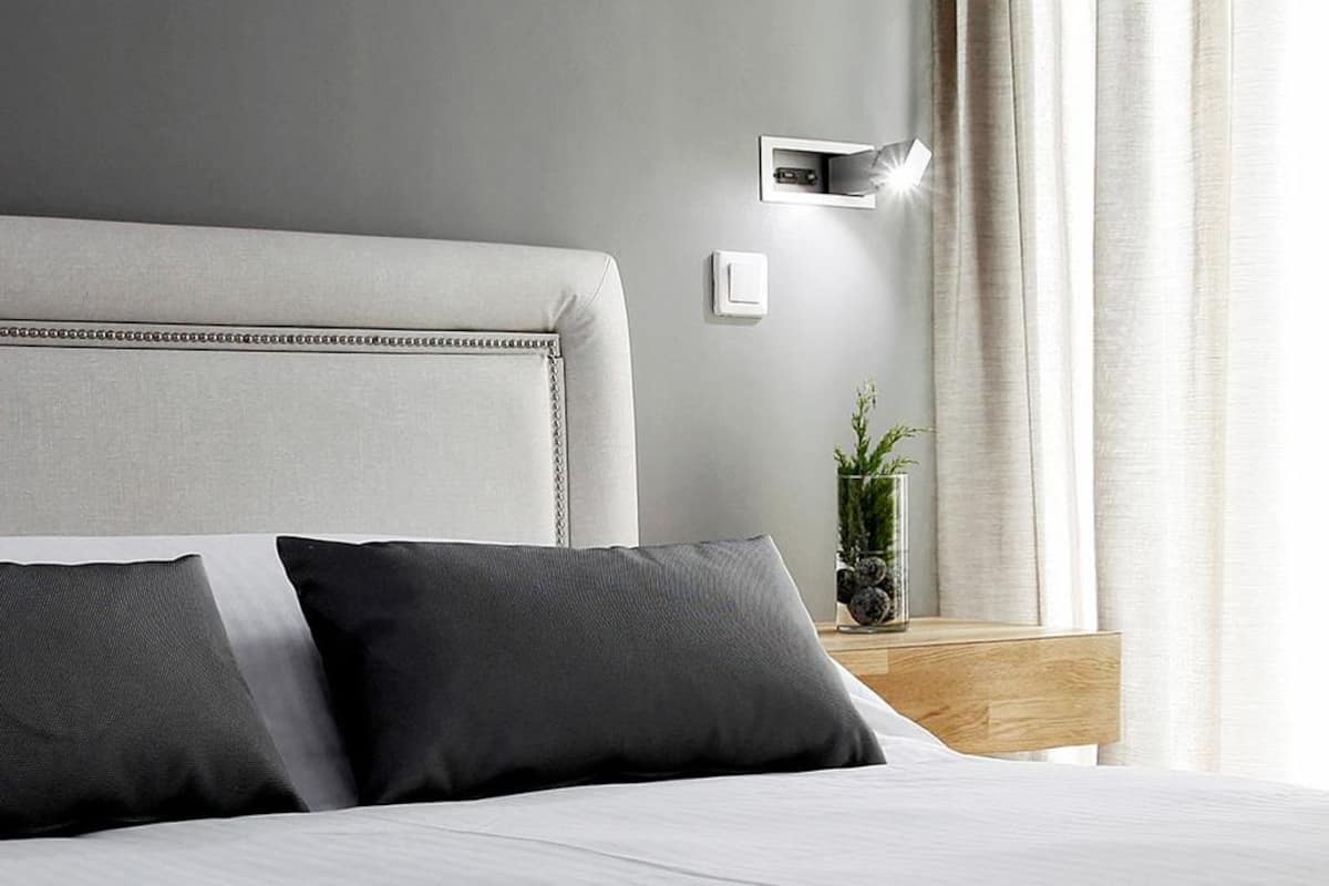 A modern hotel room with a large bed, a bedside table with a lamp, and a view of the outdoors.