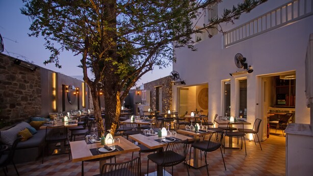 Un espacio exterior para comer con mesas y sillas, un árbol y un muro de piedra.