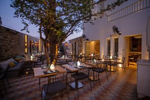Un espacio exterior para comer con mesas y sillas, un árbol y un muro de piedra.