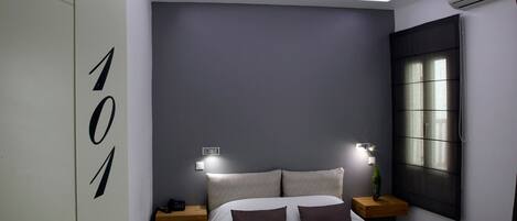 A modern bedroom with a bed, nightstands, and a wall-mounted air conditioner.