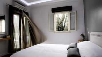 A bedroom with a bed, a window with curtains, a bedside table, and an air conditioning unit.
