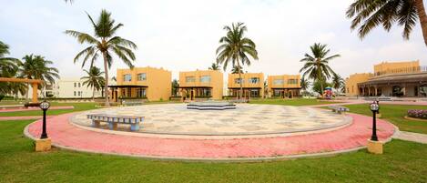 A courtyard with a circular seating area, palm trees, and buildings with yellow facades.