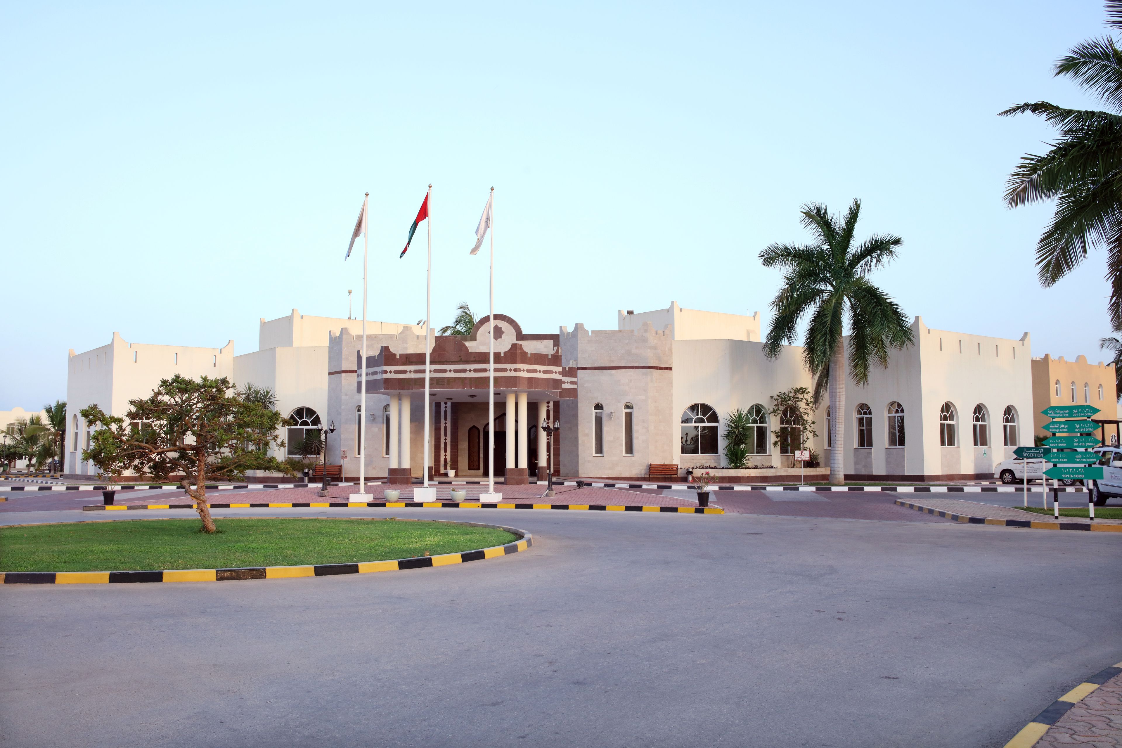 A large building with a central entrance, palm trees, and flags.