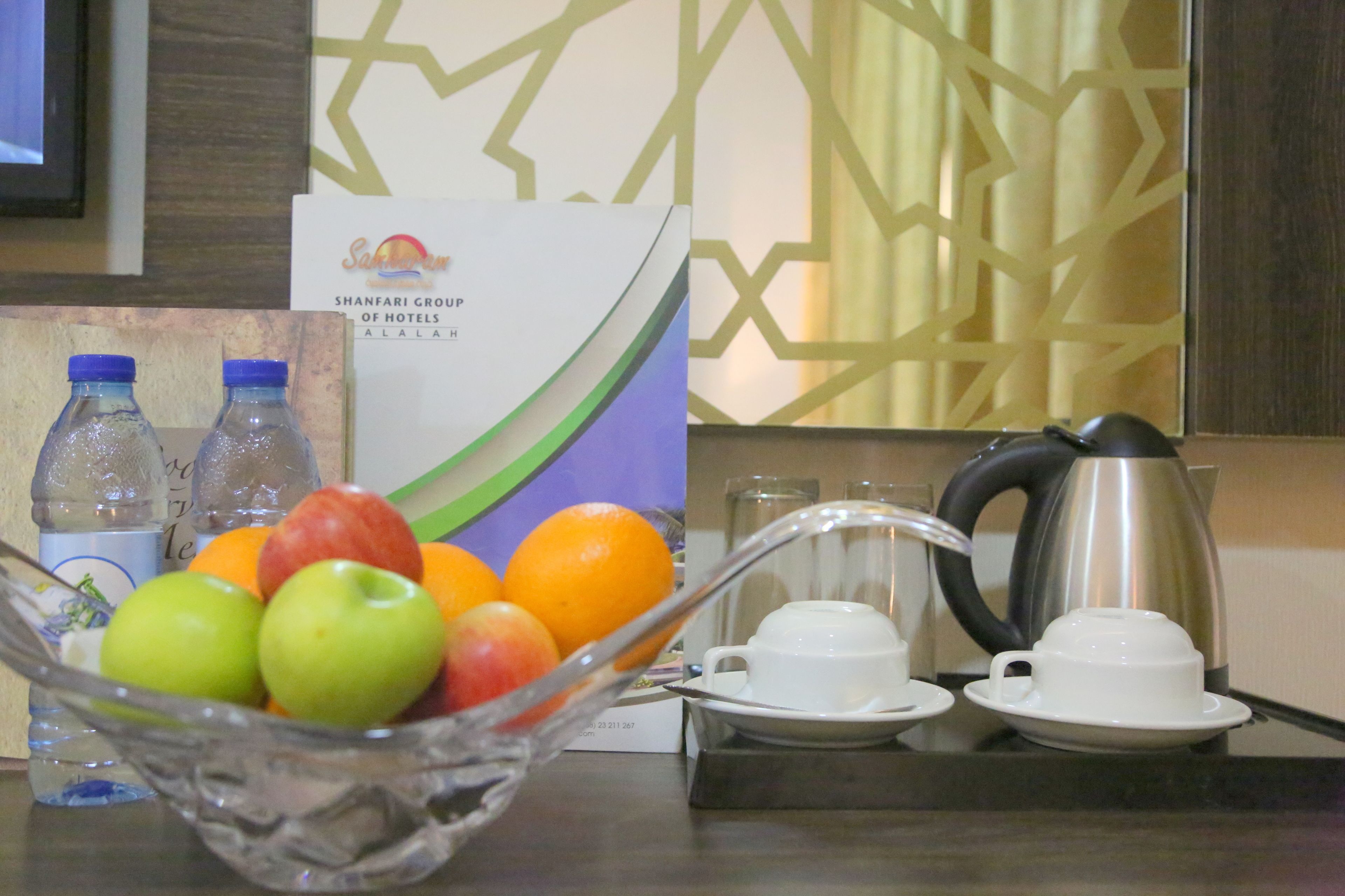 Une chambre d’hôtel avec un panier de fruits contenant des pommes et des oranges, une machine à café et deux bouteilles d’eau.