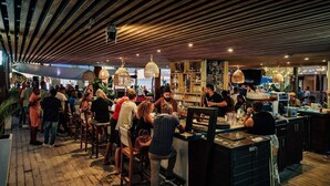 A bar area with wooden ceiling slats, hanging lights, and a bar counter with stools. - Eden Beach Resort (Kralendijk)