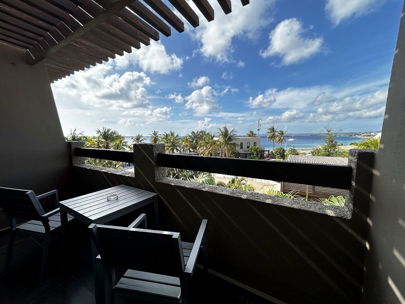 A balcony with a view of the beach, palm trees, and a clear sky.