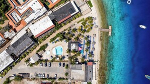 An aerial view of a coastal property with a swimming pool, parking area, and beach access. - Eden Beach Resort (Kralendijk)
