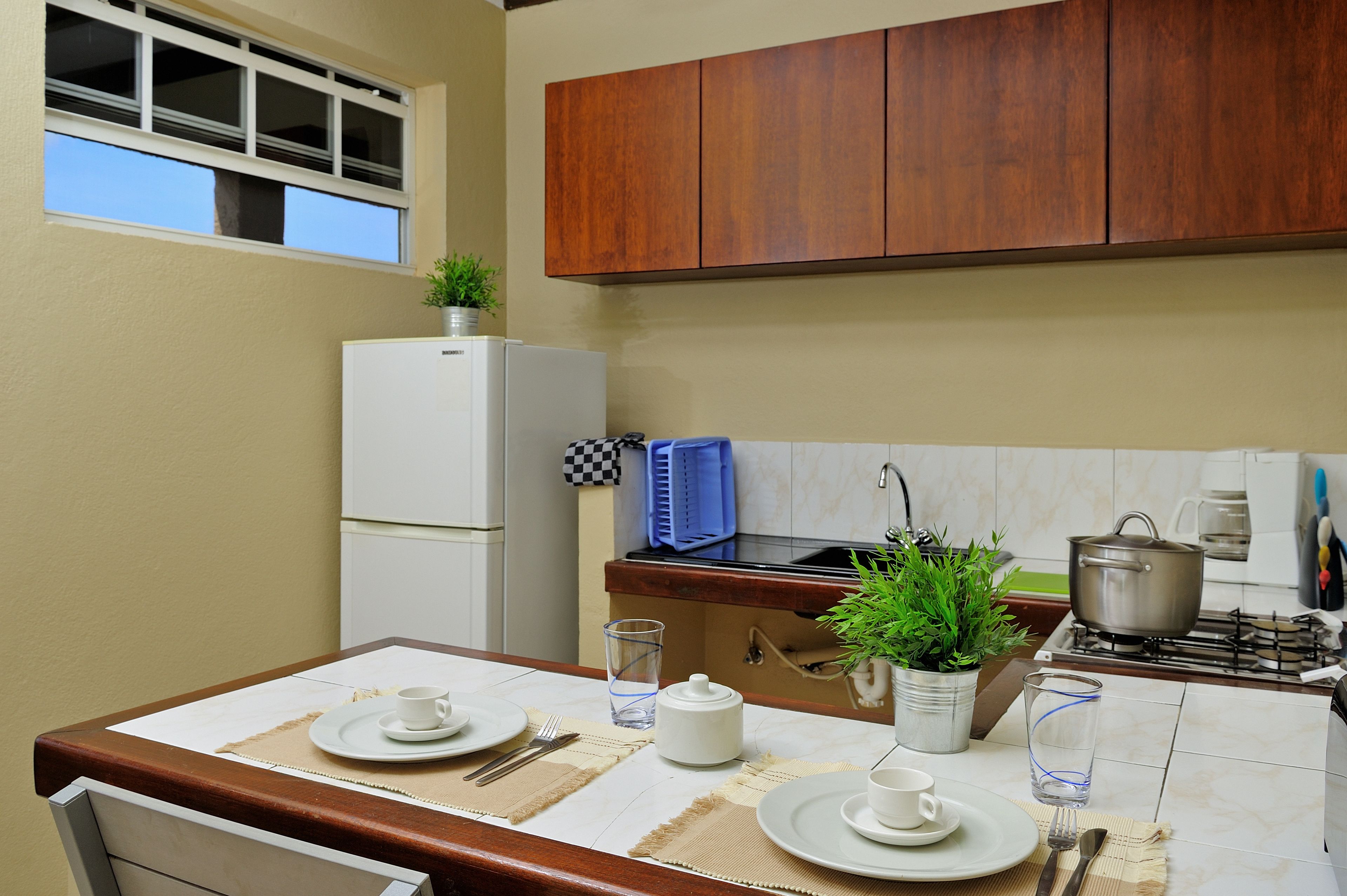 Una cucina con mobili in legno, un frigorifero bianco, un fornello e un tavolo da pranzo apparecchiato con piatti, tazze e posate.
