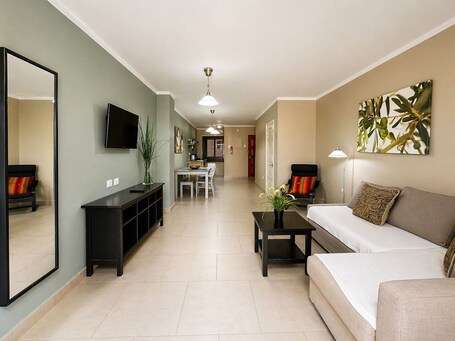 A modern living room with a sofa, a TV, a dining area, and a kitchen in the background.