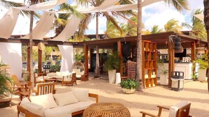 A beachside lounge with wicker furniture, palm trees, and a bar area. - Eden Beach Resort (Kralendijk)