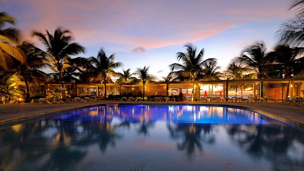 A pool with a reflection of palm trees and a sunset in the background. - Eden Beach Resort (Kralendijk)