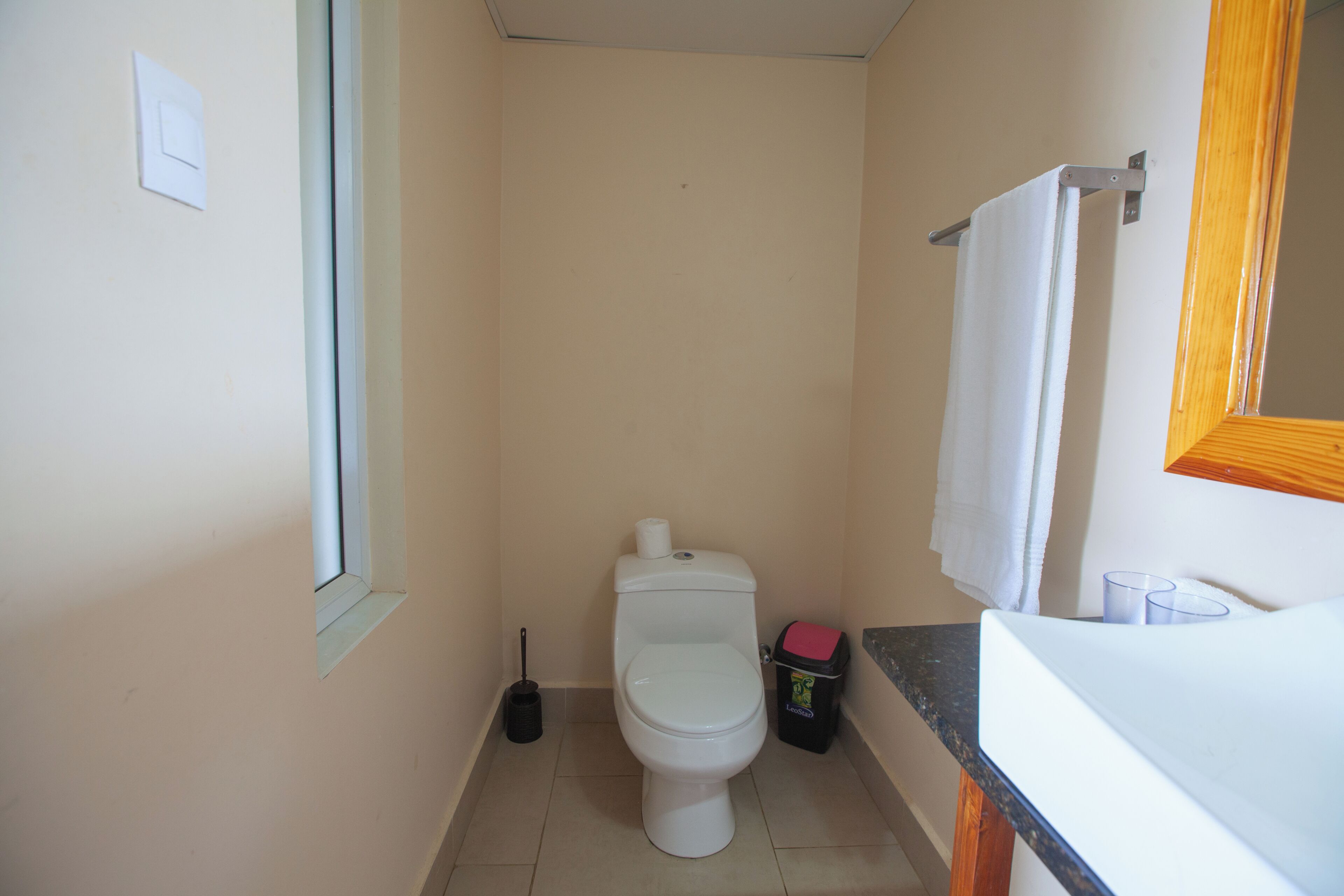 Une petite salle de bain avec des toilettes, une poubelle, une fenêtre et un lavabo.