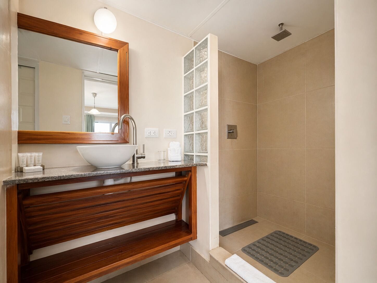 A bathroom with a wooden vanity, a large mirror, a white sink, and a shower area.