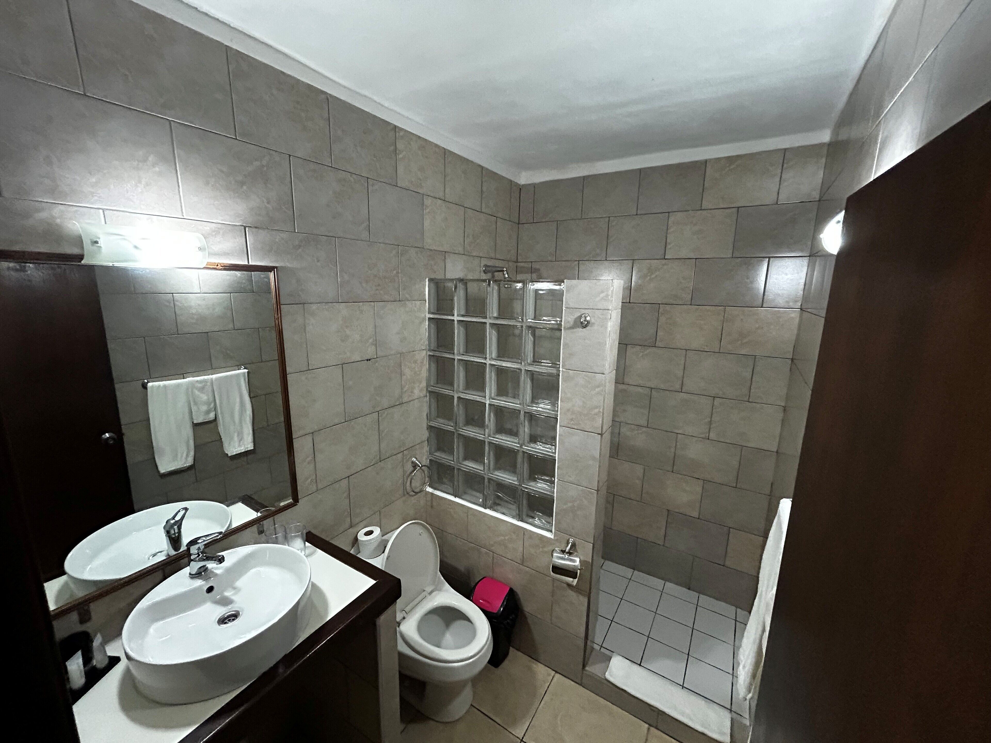 A bathroom with two sinks, a toilet, a glass shower enclosure, and a mirror.