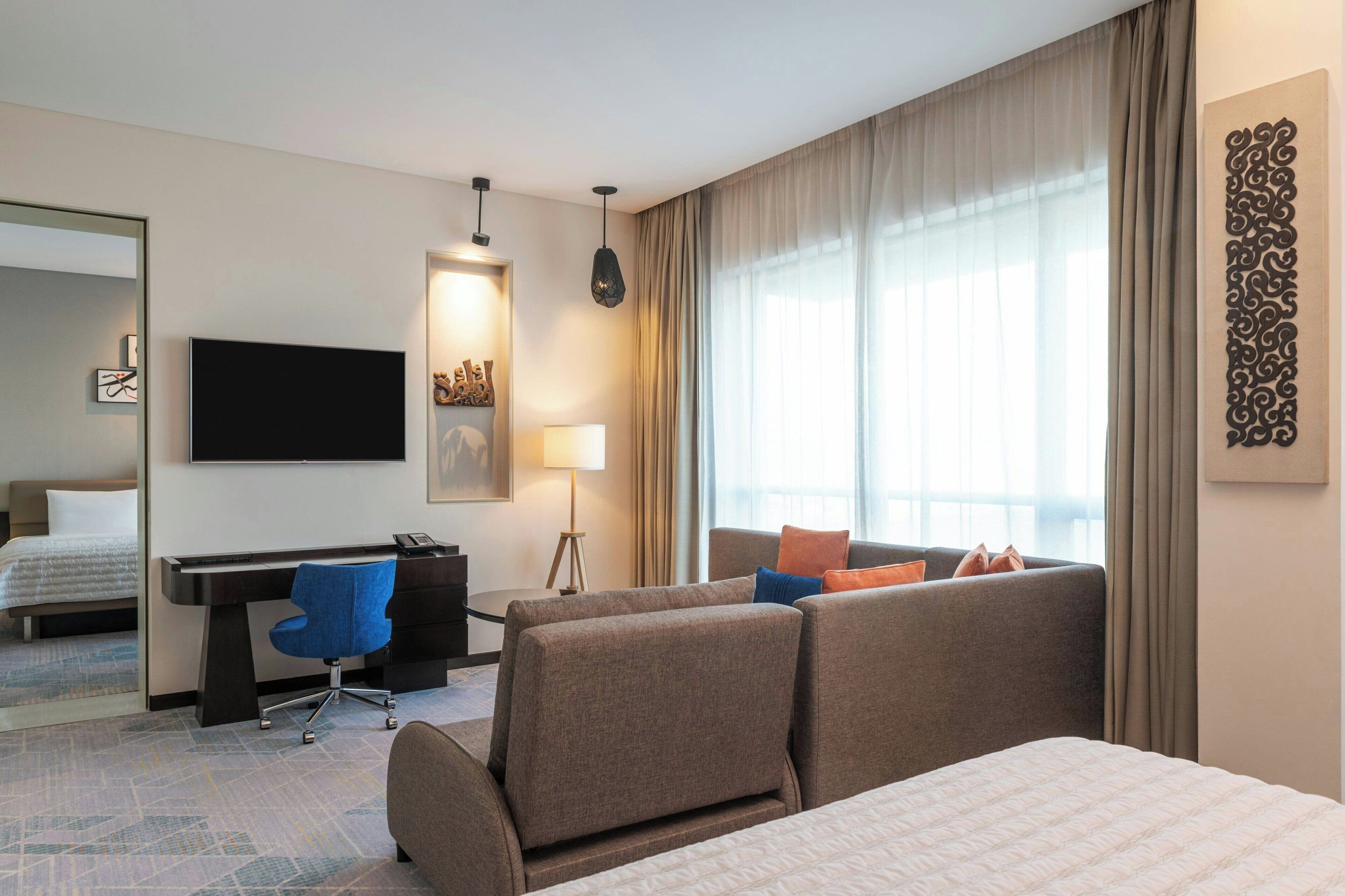 A hotel room with a bed, a desk with a chair, a TV, and a sofa.