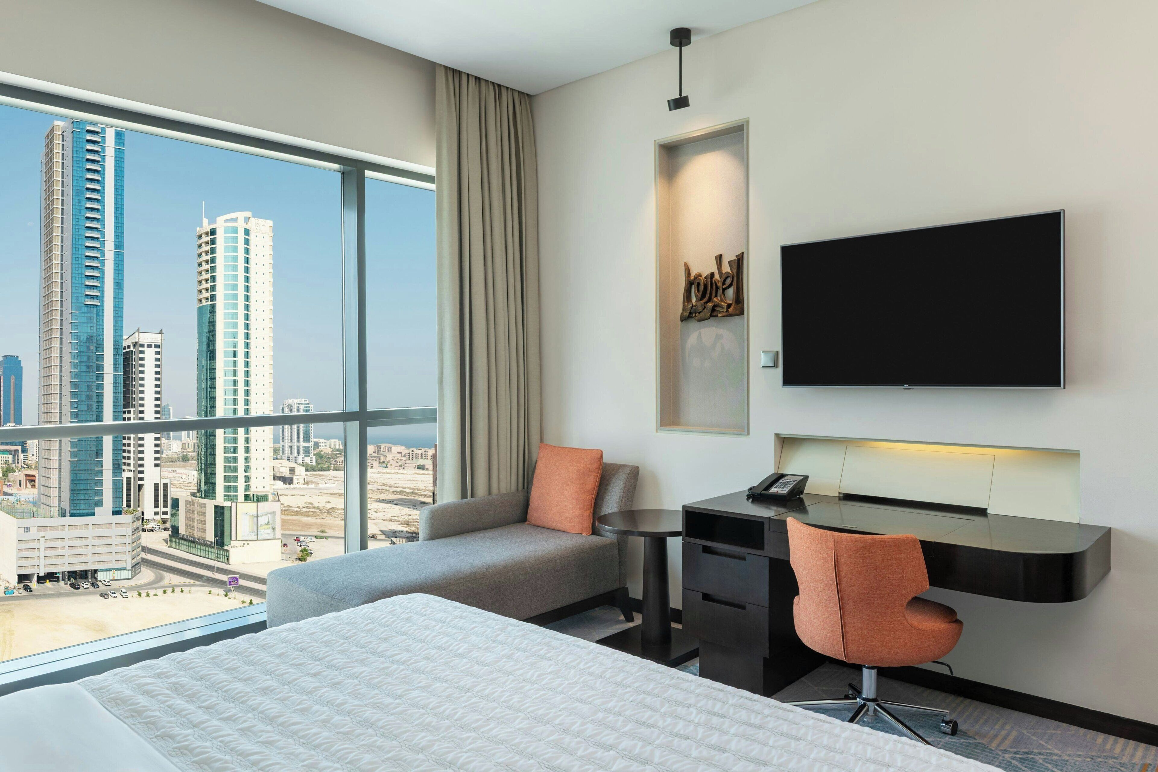 Une chambre d’hôtel avec un lit, un bureau, une chaise, une télévision et une vue sur la ville.