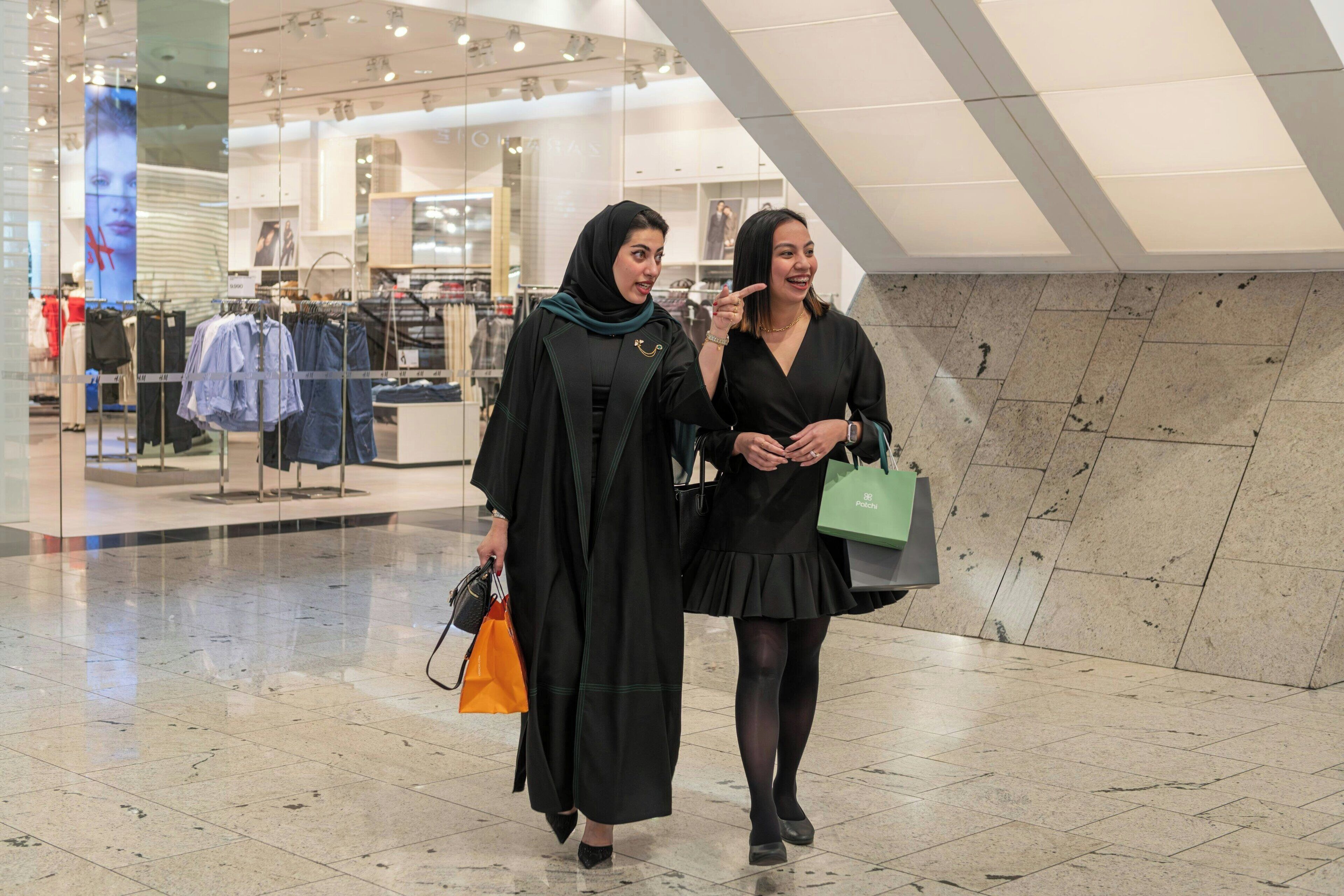 Two people walking inside a shopping mall with a clothing store in the background.