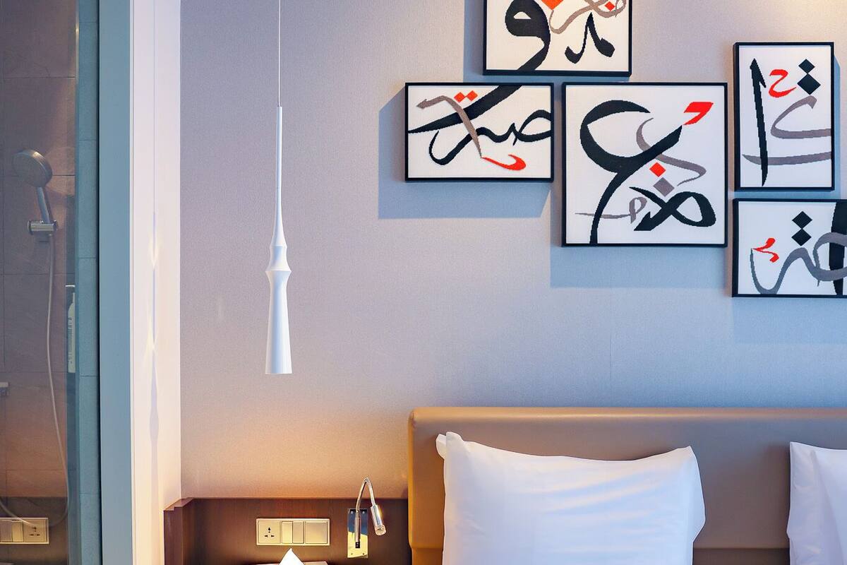 A hotel room with a bed, a round bedside table, a wall-mounted artwork, and a hanging light fixture.
