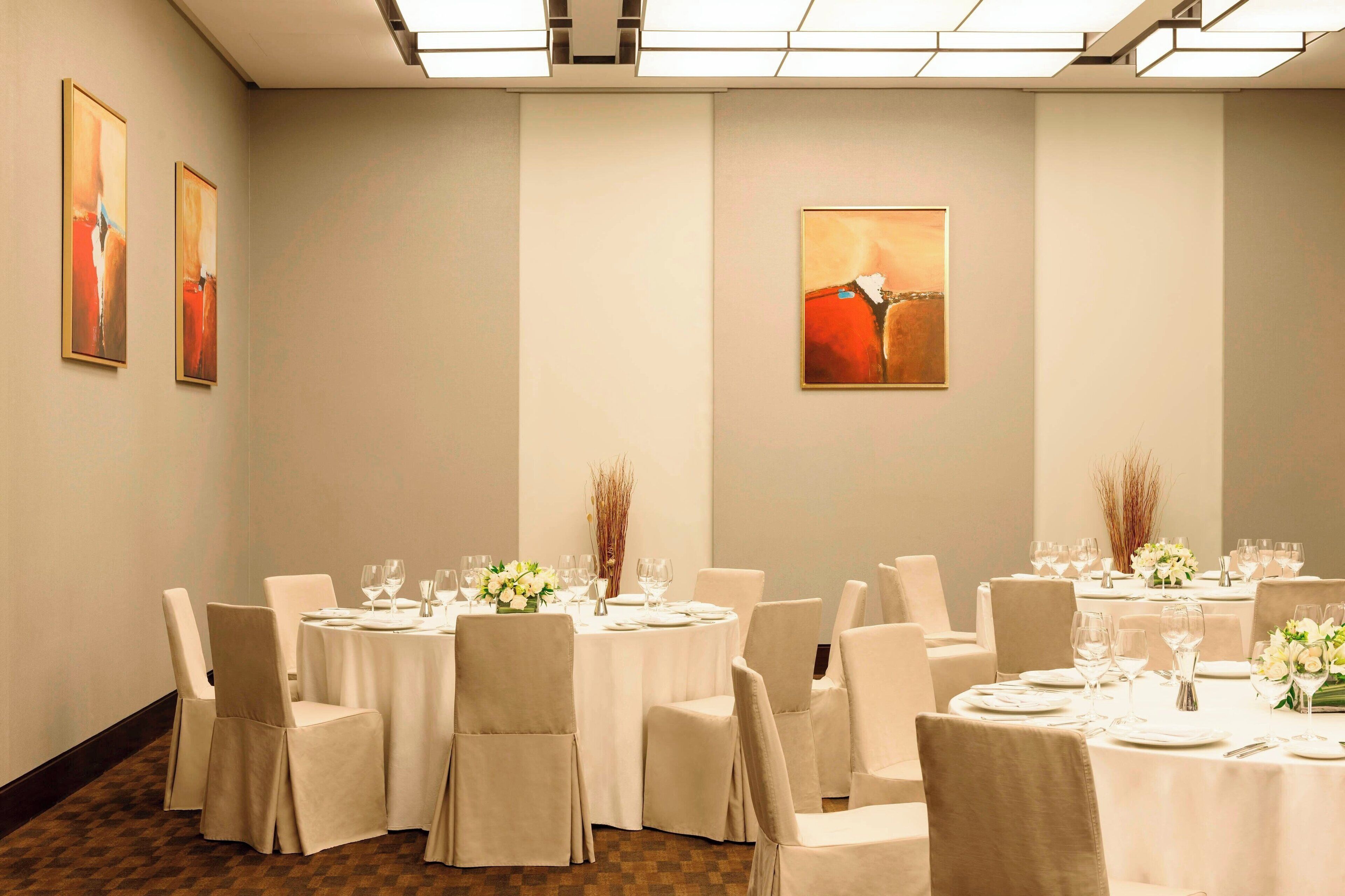 Un salón de conferencias con mesas redondas, sillas blancas y obras de arte en las paredes.