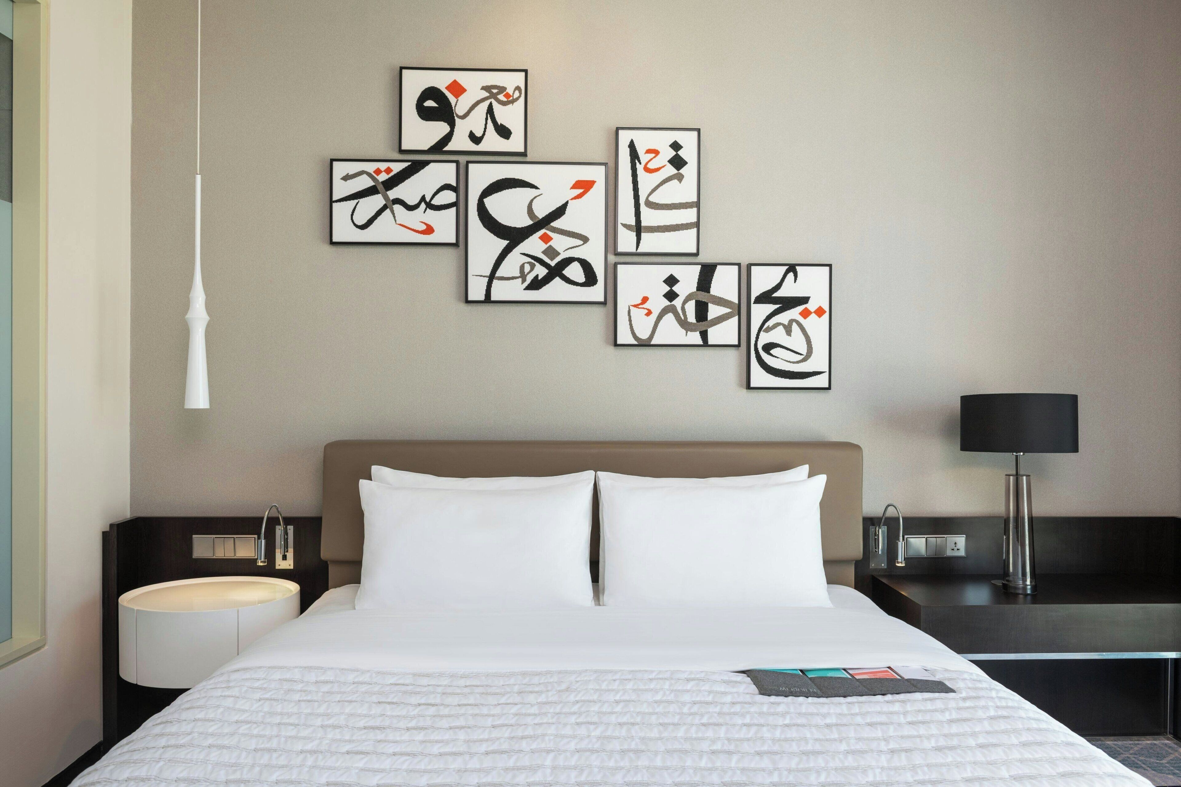 Ein Hotelzimmer mit einem großen Bett, einem Nachttisch mit Lampe, einem Wandbild und einem Beistelltisch mit Lampe.