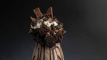 A dessert in a glass with chocolate and Oreo pieces on top.