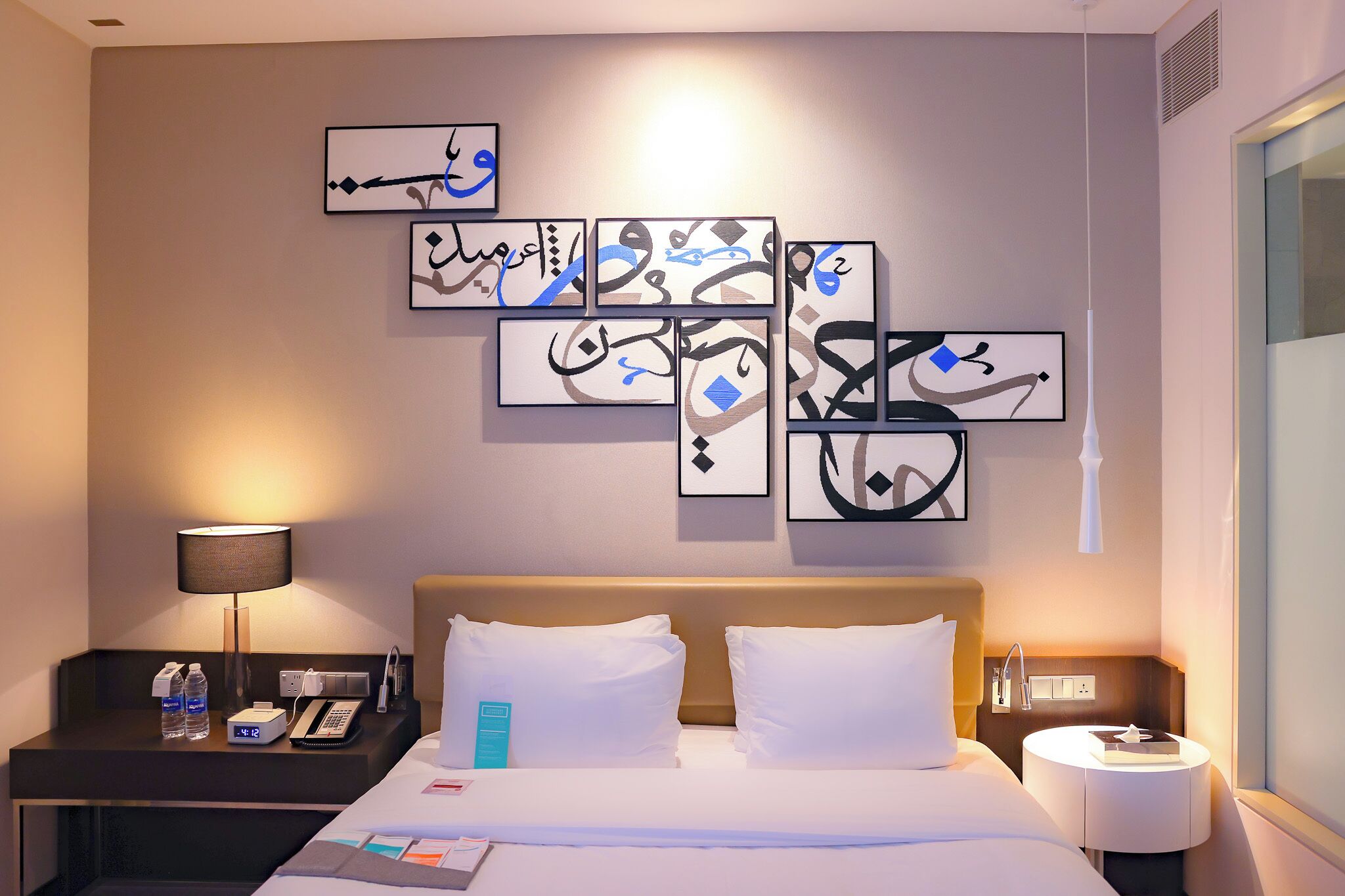 A hotel room with a bed, bedside tables, a wall with framed artwork, and a window.