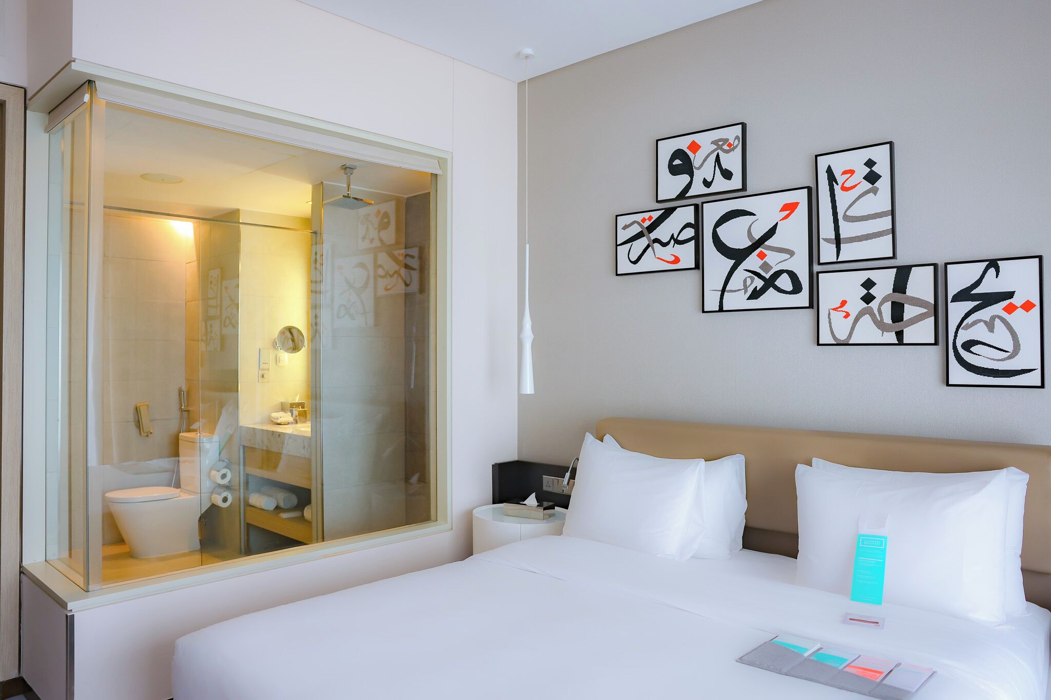 Habitación de hotel con una cama grande, una mesita de noche y un baño con cabina de ducha de vidrio, además de una obra de arte en la pared.