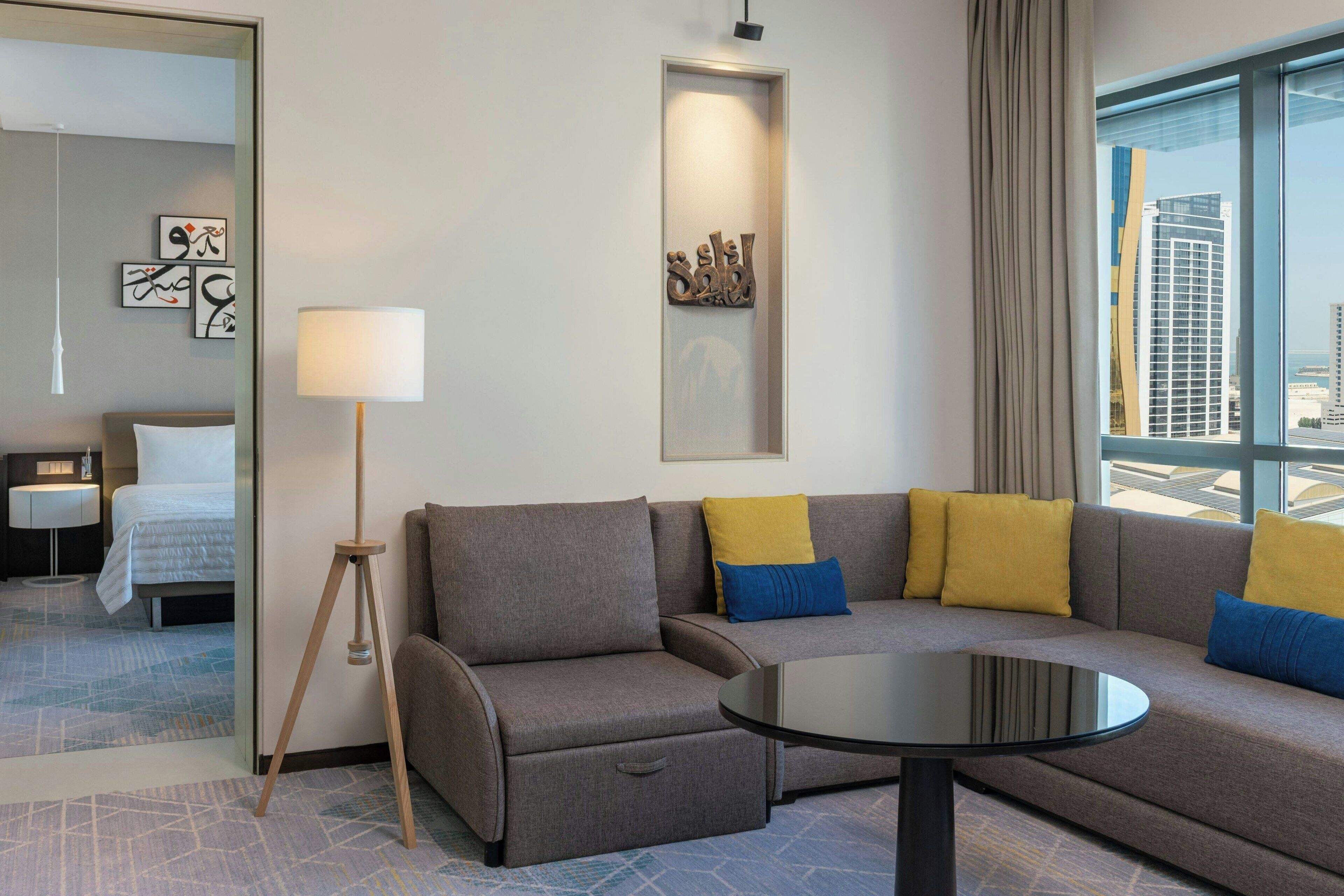 A modern hotel room with a sofa, a round table, a lamp, and a bed.