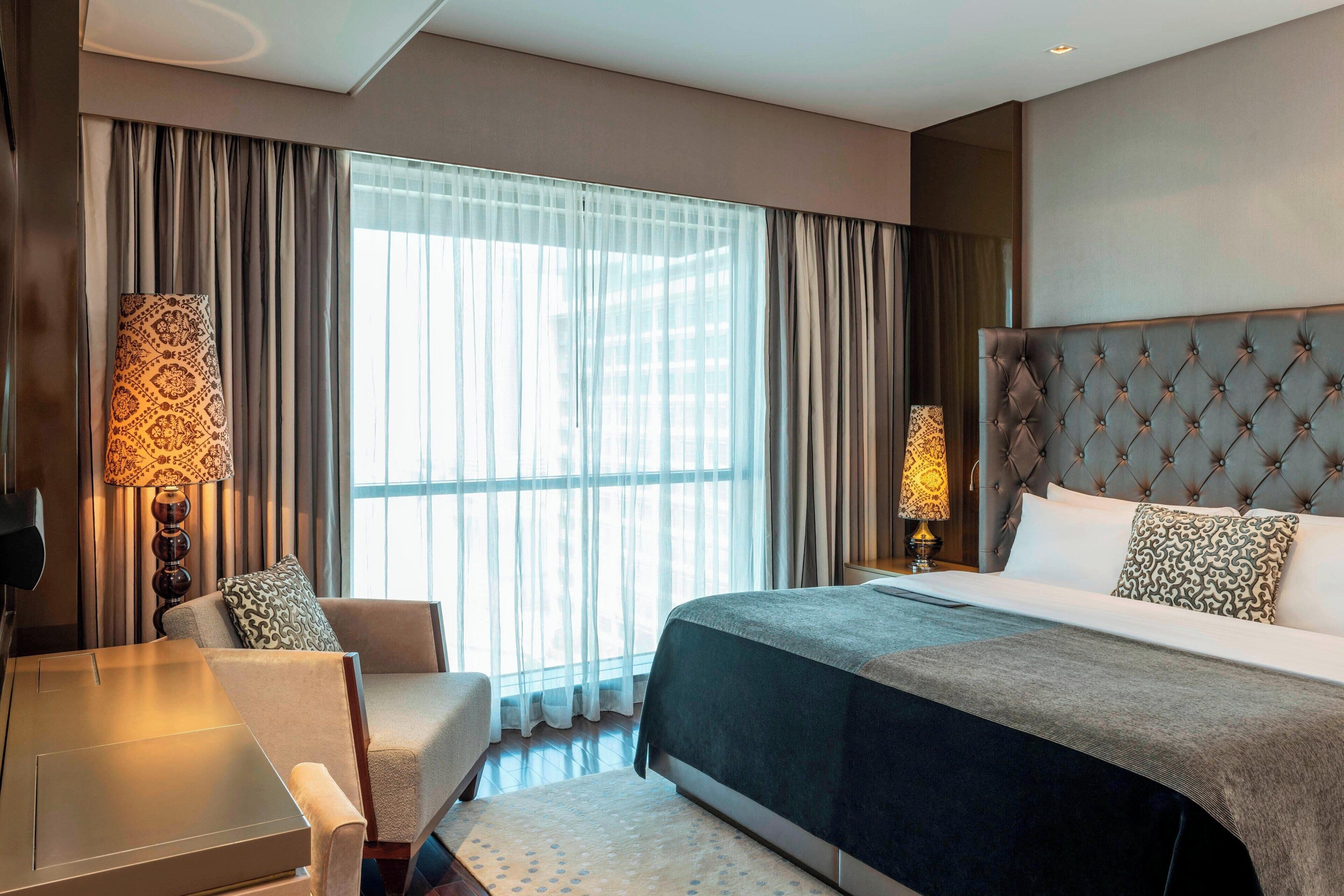A hotel room with a large bed, a sofa, a desk, and a window with curtains.