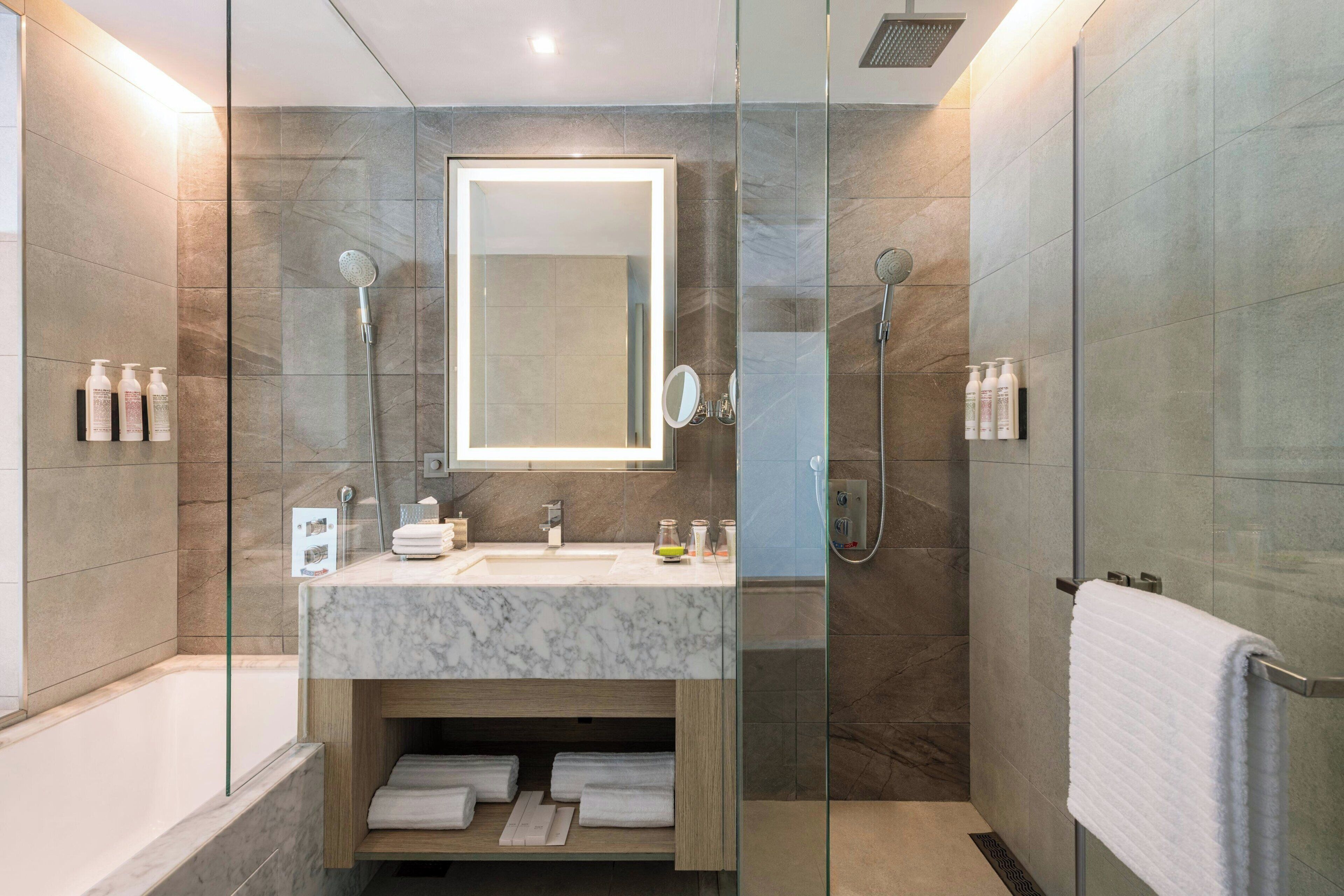 A modern bathroom with a glass-enclosed shower, a marble sink, and a built-in mirror.