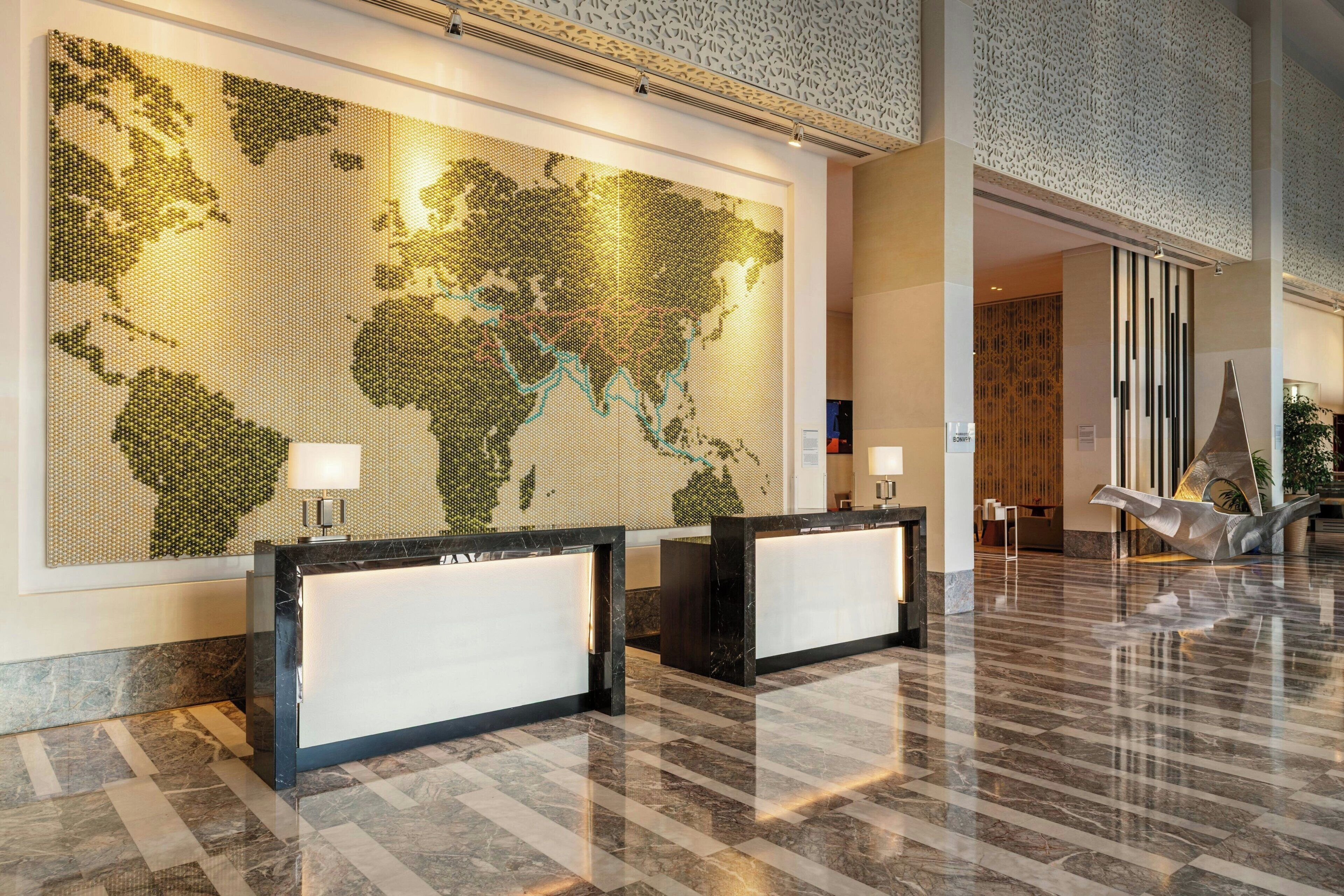 Een lobby met een groot wereldkaart-muurdecor, twee receptiebalies en een gepolijste marmeren vloer.