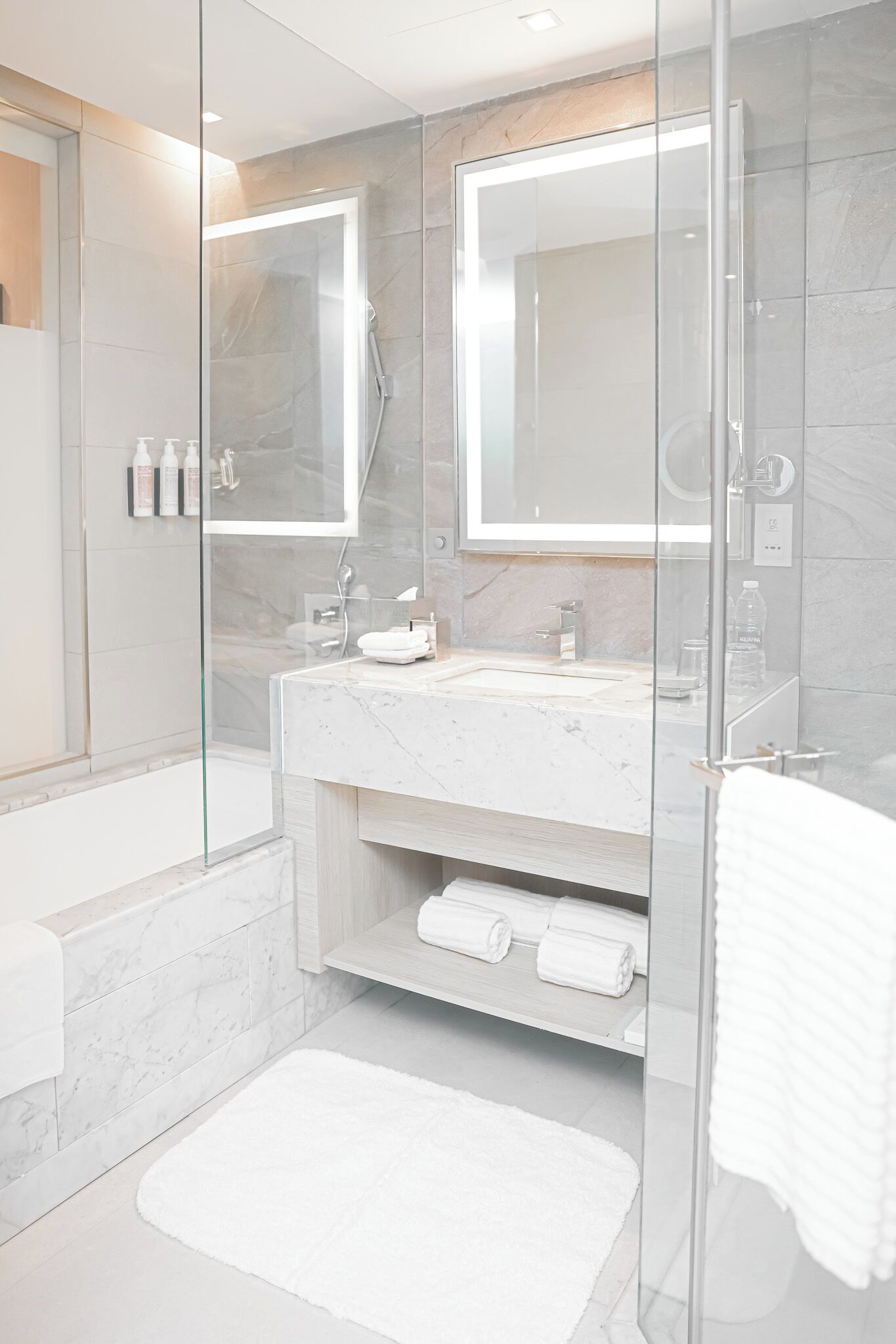 Une salle de bain moderne avec une douche à parois de verre, un lavabo en marbre et un grand miroir.