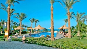 A resort pool area with palm trees, lounge chairs, and umbrellas. - Tamra Beach Resort (Sharm El Sheikh)
