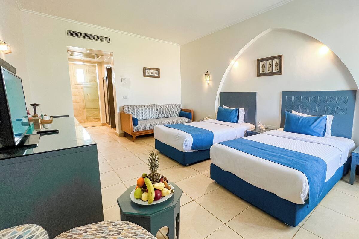 A hotel room with two beds, a desk, a chair, and a fruit bowl.