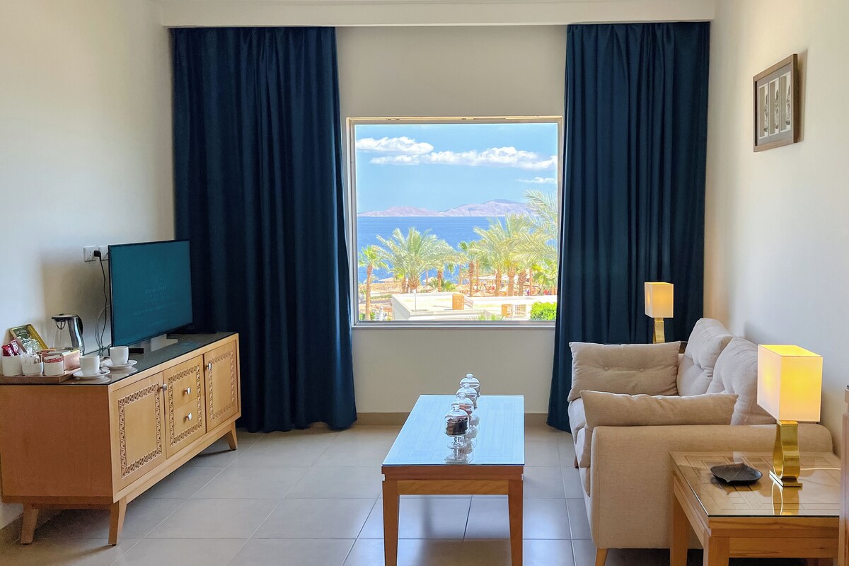 A hotel room with a large window, a sofa, a coffee table, a TV, and a cabinet.