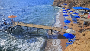 Une plage avec une jetée en bois, des parasols bleus et blancs, et des chaises longues.