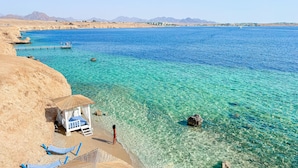 Ein Strand mit klarem türkisblauem Wasser, einer Reetdachhütte und ein paar Hängematten.