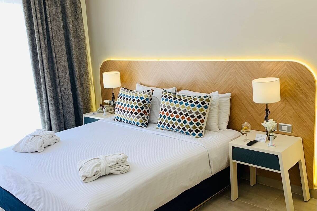 A hotel room with a large bed, two bedside tables, and a headboard with built-in lighting.
