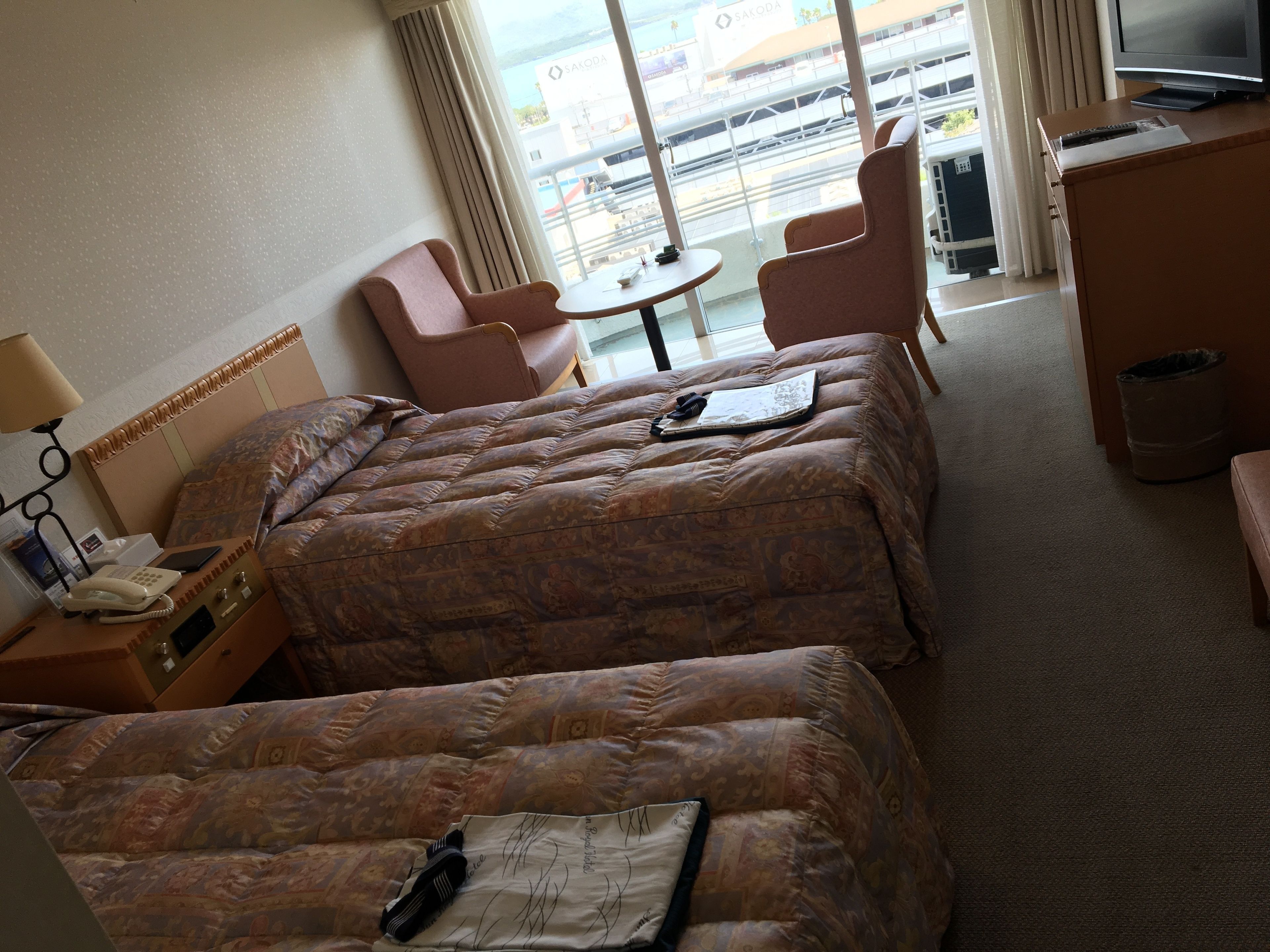A hotel room with two beds, a desk with a telephone, a chair, a small table, and a TV.