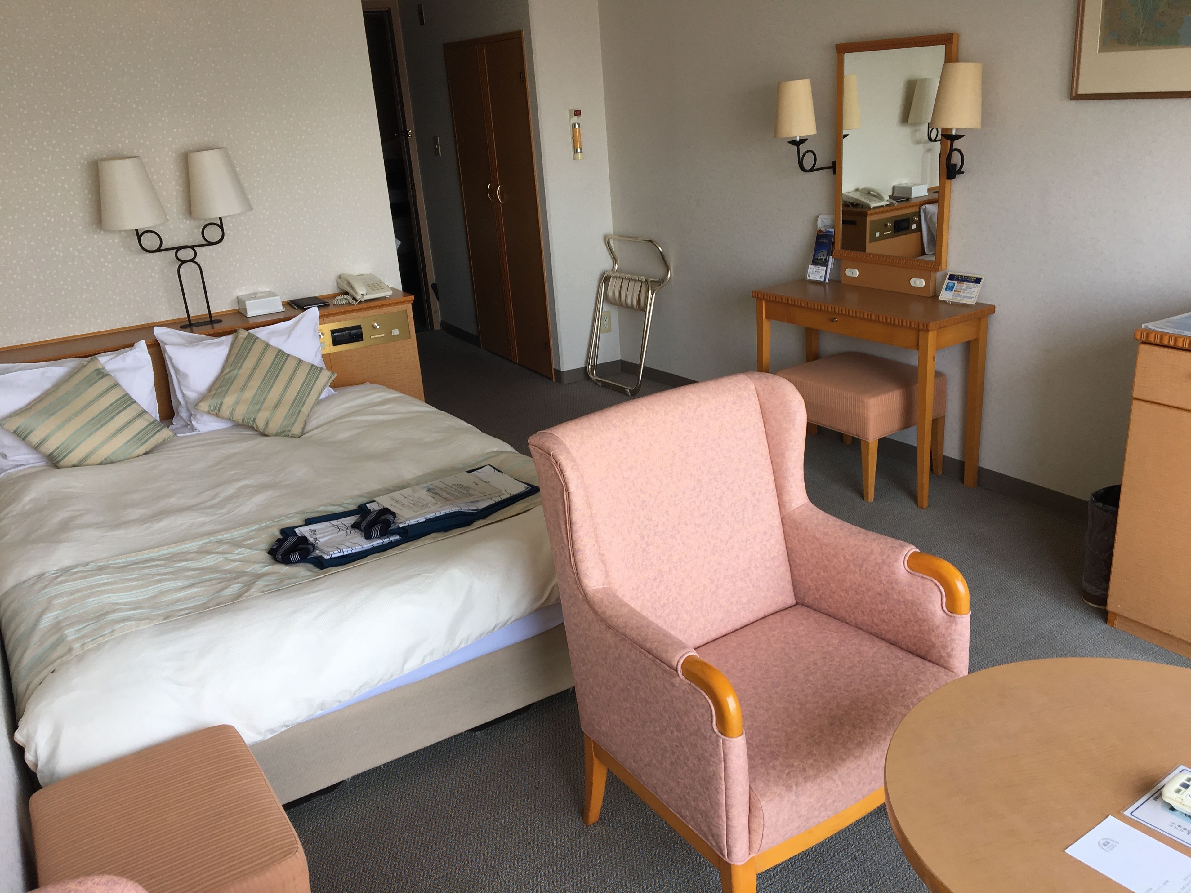 Habitación de hotel con cama, escritorio, silla, mesita, espejo y lámpara.