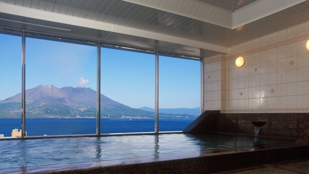 A modern indoor pool with a large window view of a volcano and sea. - Kagoshima Sun Royal Hotel (Kagoshima)
