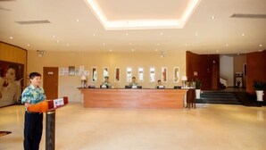 A hotel reception area with a wooden reception desk, several framed certificates on the wall, and a large poster. - Herton Seaview Hotel (Sanya)