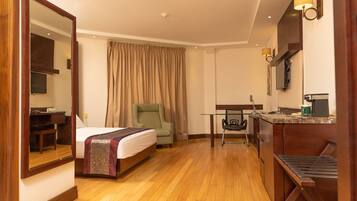 Habitación de hotel con cama, escritorio, silla, mesita, espejo y televisión.