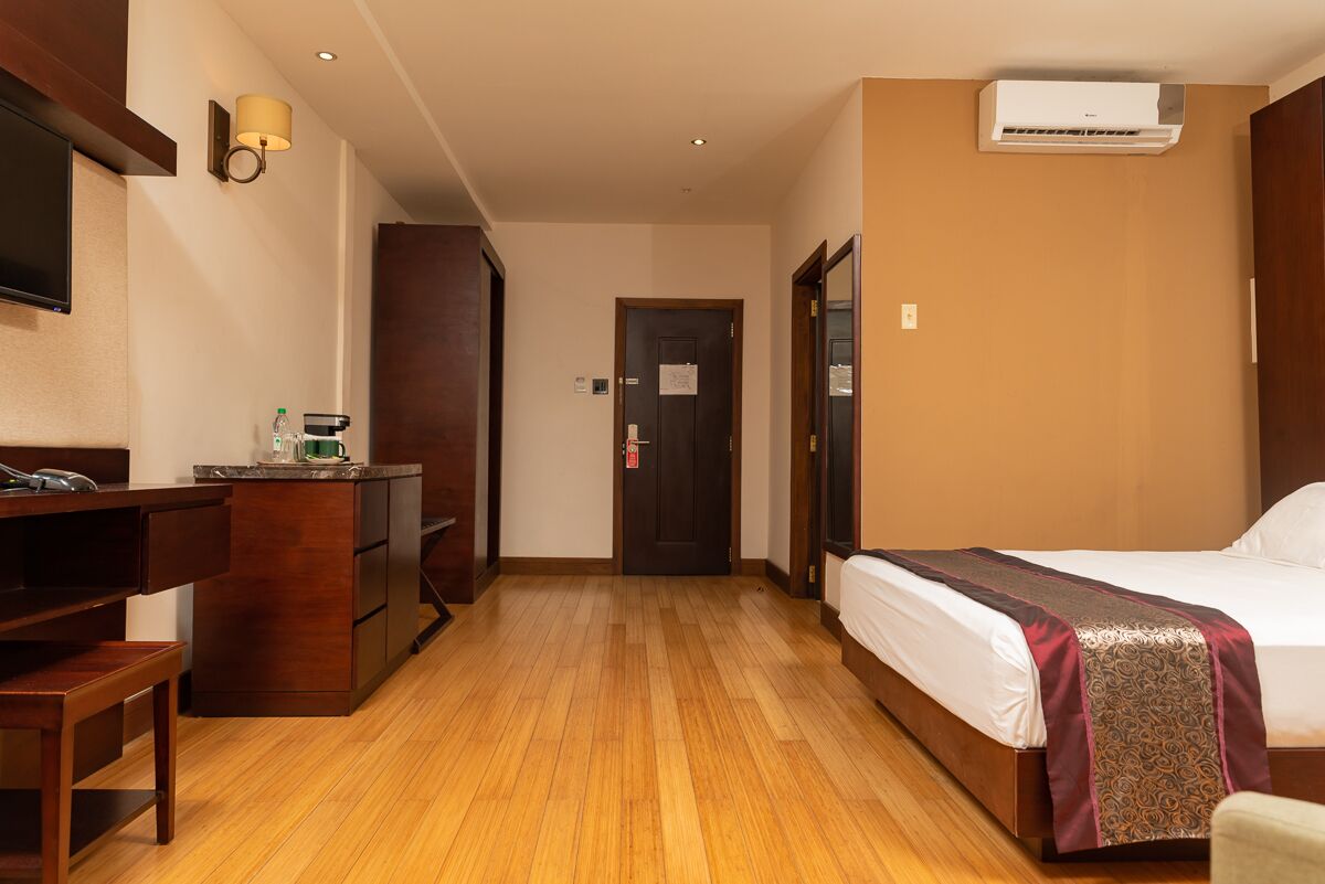 Una habitación de hotel con piso de madera, una cama con colcha estampada, un escritorio con silla, un televisor montado en la pared y un equipo de aire acondicionado.